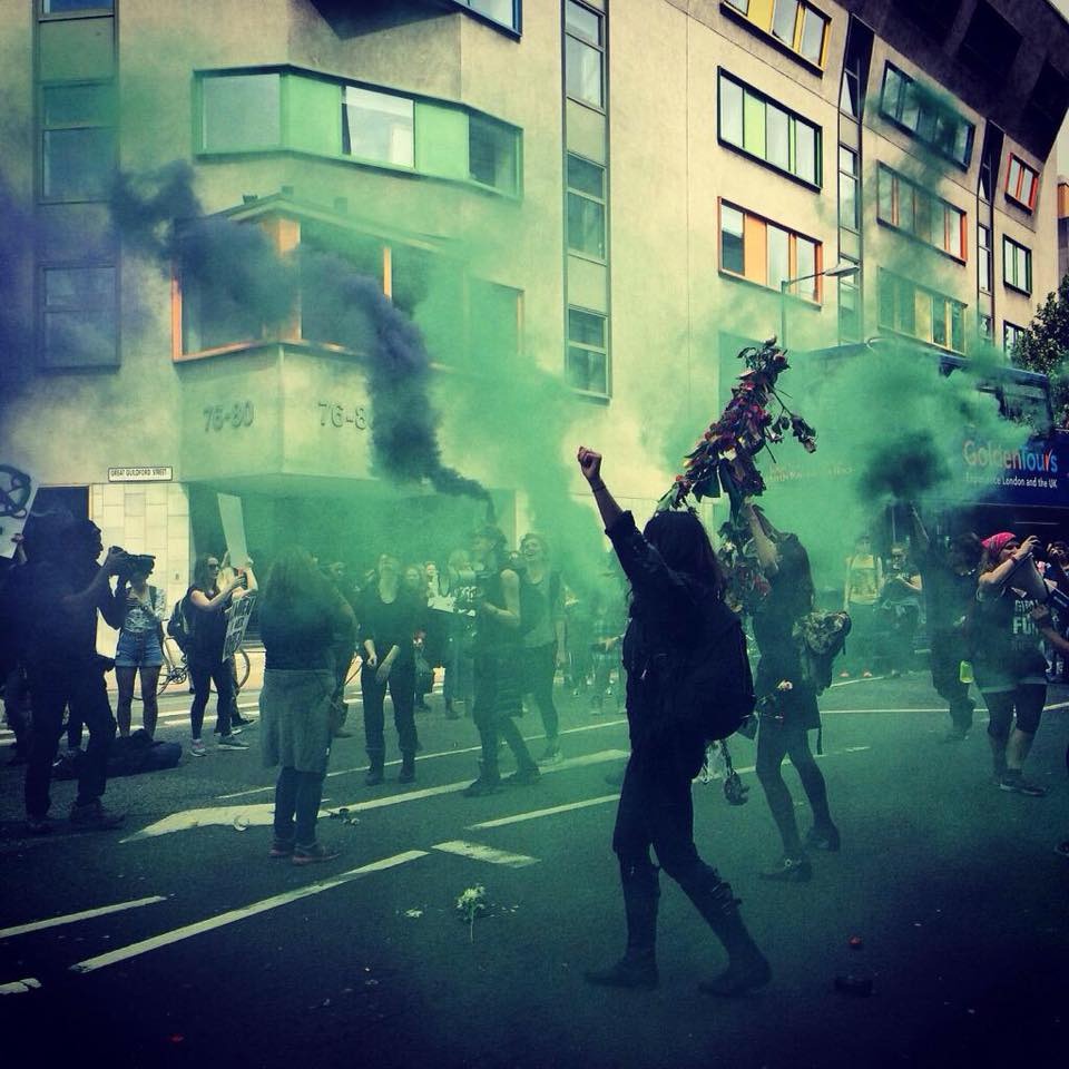 A woman dances in the middle of a protest while green flares go off around her.